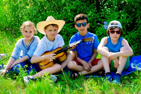 Group of cheerful children resting in the park with songs and guitar. Outdoor activity. Summer...