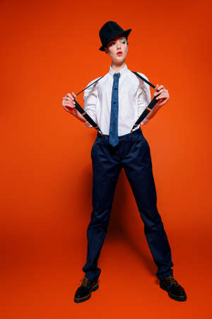 Fashion shot. Attractive young model posing in a man's suit and bowler hat. Man's style clothing. Red background.の写真素材