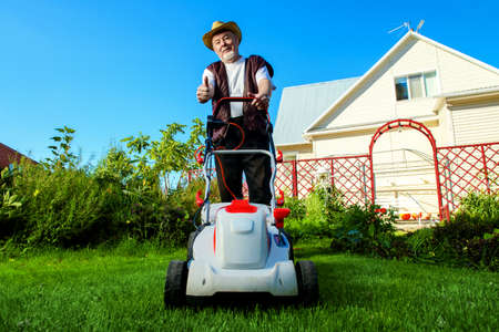 Happy retired senior man mows a lawn in his garden with a lawnmower.の写真素材