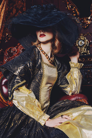 Portrait of a beautiful young woman in the lush expensive dress and elegant broad-brimmed hat in an...