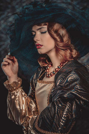 Fashion shot of a stunning young woman in luxurious dress and elegant hat over vintage background. Headwear style.の写真素材