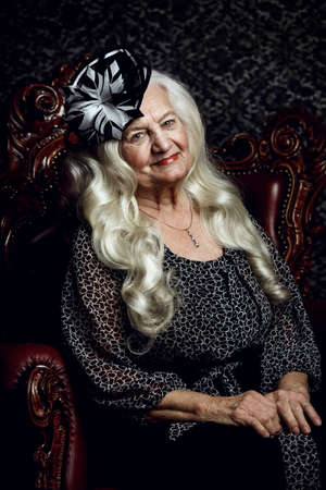 Fashionable old woman with beautiful blonde hair and elegant hat posing in vintage interior. Beauty, fashion. Retro style.の写真素材