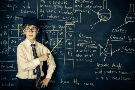Cute schoolboy answers by a blackboard on a chemistry lesson. Educational concept.