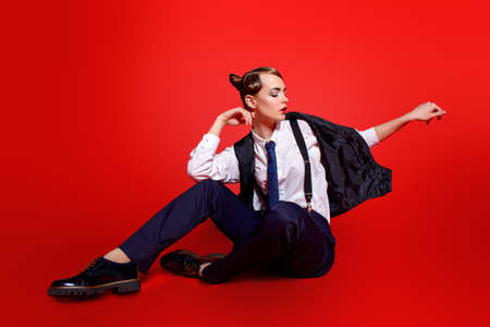 Fashion shot. Attractive young woman posing in a man's shirt and trousers with suspenders. Man's style clothing. Red background.の写真素材