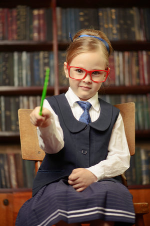 Cute girl looking like a teacher sits in the library with her pointer. Educational concept.の写真素材