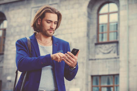 Young businessman walking down the street and using his smartphone. Lively active lifestyle.の写真素材