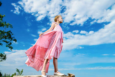 Happy little girl in beautiful long dress over blue sky. Children's fashion. Happy summer holidays.の写真素材