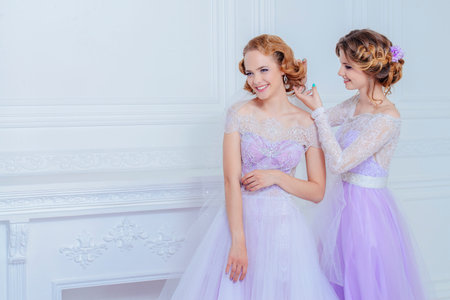 Charming bride and bridesmaid stand together in beautiful dresses and smile. Wedding fashion.