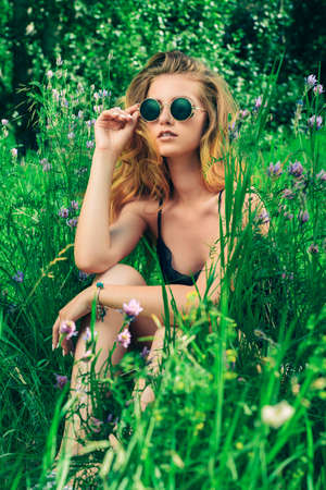 Pretty girl sits in the grass among the wild flowers. Summer day. Modern hippie, hipster style. Beauty, fashion outdoor.の写真素材