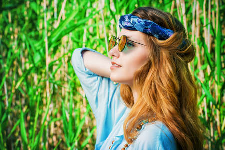 Beautiful hippie girl stands among the reeds in a summer sunny day. Spirit of freedom. Fashion shot. Bohemian, bo-ho style.の写真素材