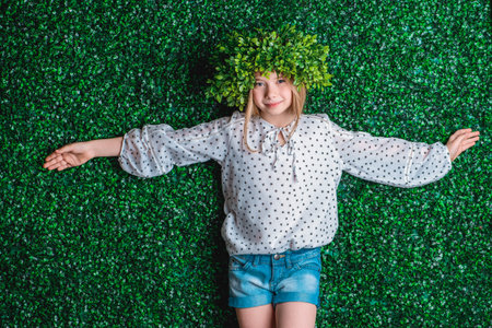 Portrait of a beautiful summer girl wearing green wreath in a green summer garden. Children's...