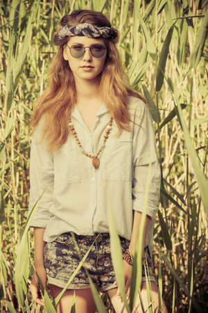 Beautiful hippie girl stands among the reeds in a summer sunny day. Spirit of freedom. Fashion shot. Bohemian, bo-ho style.の写真素材