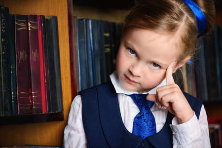 Portrait of a cute little girl standing by bookshelves in the library. Educational concept.の写真素材