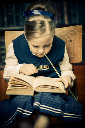 Cute girl looks curiously into the book in a library. Educational concept.の写真素材
