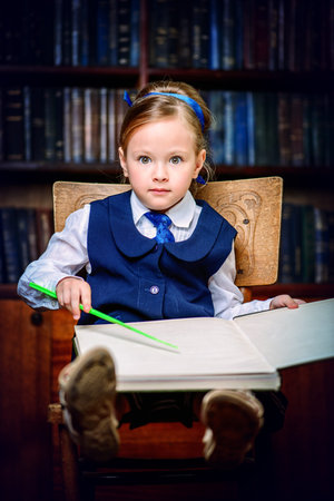 Cute little girl sitting with opened book in a library. Educational concept.の写真素材
