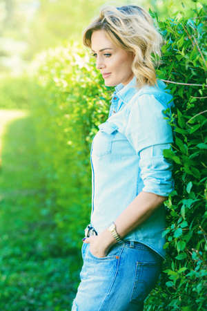 Beautiful middle aged woman is standing by the green hedge in the park on a summer day. Beauty, cosmetics.の写真素材