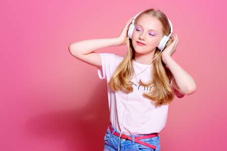 Portrait of a cute modern girl teenager with headphones over pink background.の写真素材