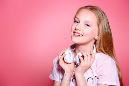 Portrait of a cute modern girl teenager with headphones over pink background.の写真素材