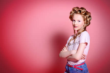 Portrait of a pretty girl teenager with curlers in her blonde hair. Studio shot over pink background.の写真素材