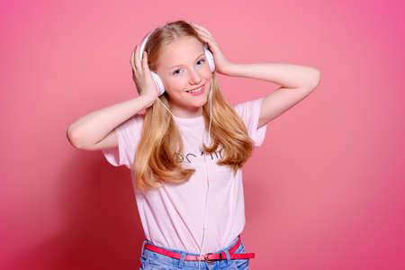 Portrait of a cute modern girl teenager with headphones over pink background.の写真素材