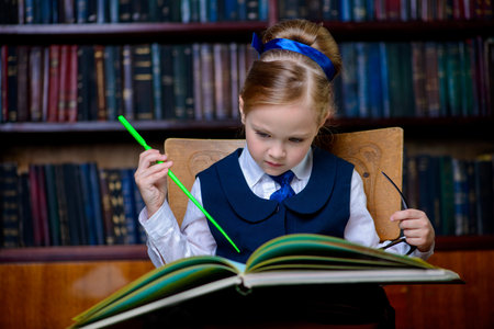 Cute girl looks curiously into the book in a library. Educational concept.
