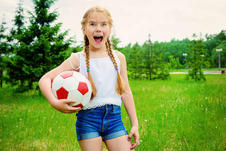 Happy girl plays with a ball in a summer park.の写真素材