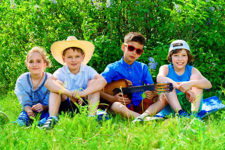 Group of cheerful children resting in the park with songs and guitar. Outdoor activity. Summer holidays.の写真素材
