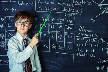 Puzzled schoolboy stands by a blackboard on a chemistry lesson. Educational concept.の写真素材