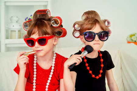 Two funny little girls with curlers in their hair make themselves a make-up. Kid's fashion. Family at home.の写真素材