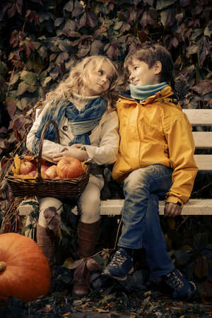 Happy romantic boy and girl sitting on a bench in a beautiful autumn park. Children's fashion. Autumn mood, halloween.の写真素材