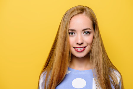 Joyful young woman with beautiful smile posing over yellow background.