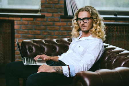 Young handsome businessman is working at home using his laptop. Male beauty, fashion. Business style. Modern technologies.の写真素材