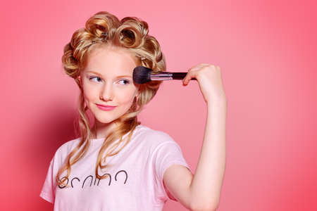 Portrait of a pretty girl teenager with curlers in her blonde hair and brushes. Teen style, fashionable teen girl. Cosmetics and make-up.の写真素材