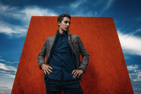 Vogue shot. Handsome fashionable man model posing outdoor over red background and a sky.の写真素材