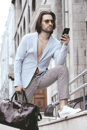 Male fashion. Modern handsome man talking on his cell phone on a city street. Summer day.の写真素材