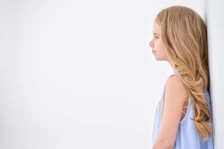 Beautiful little girl in a pale blue dress standing in a white room full of light. Kid's fashion. Hairstyle.の写真素材