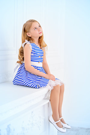 Cute little girl in a beautiful summer dress posing in a room with classical white interior. Kid's fashion.の写真素材