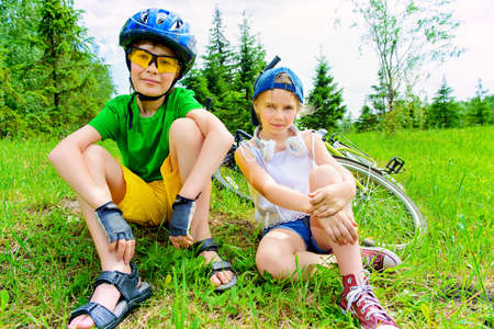 Two happy children are resting on a green lawn after riding their bikes. Happy summer holidays.の写真素材