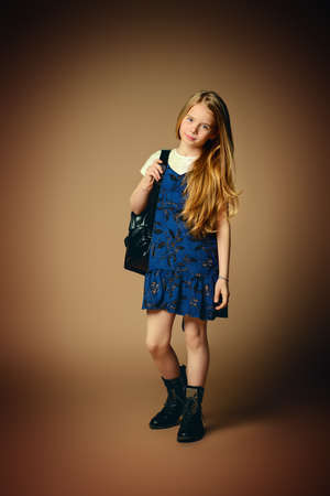 Children's fashion. Cute eight year old girl with long blonde hair posing in summer dress and a bag. Studio shot. Full length portrait.の写真素材