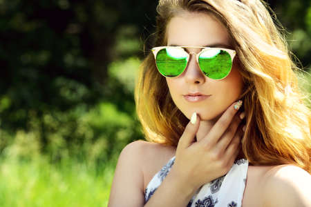 Close-up portrait of a beautiful young woman in sunglasses in a summer park. Optics style. Beauty, fashion outdoor.の写真素材