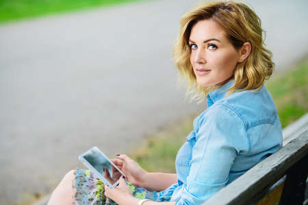 Happy middle aged woman relaxing on a bench in the park on a summer day. Mood of summer and carefree vacations. Beauty, cosmetics.の写真素材