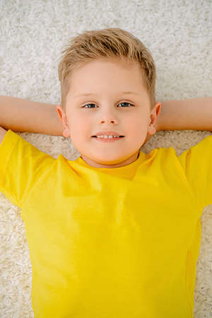 Joyful smiling child boy lying on a carpet and having a rest at home. Happy childhood.の写真素材