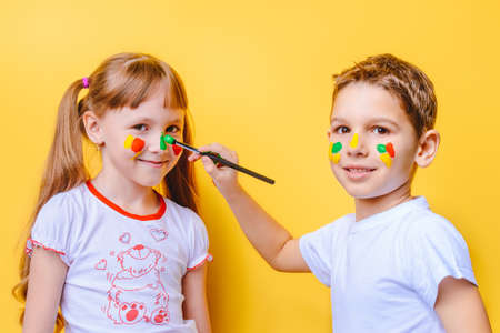 Joyful children with paints on their faces and palms. Drawing. Creativity and education concept. Yellow background.の写真素材