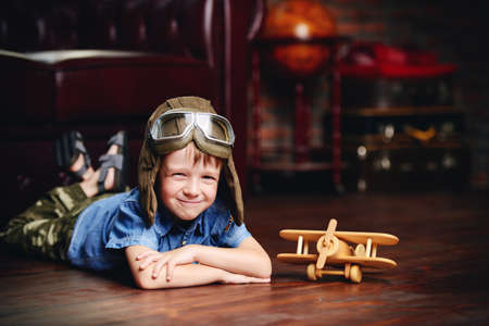 Cute dreamer boy playing with toy airplane at home. Childhood. Fantasy, imagination.の写真素材