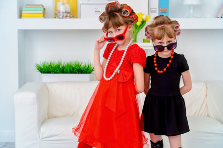 Two funny little girls with curlers in their hair make themselves a make-up. Kid's fashion. Family...