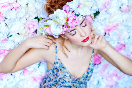 Beautiful romantic young woman in a wreath of flowers posing on a background of roses. Inspiration of spring and summer. Perfume, cosmetics concept.の写真素材