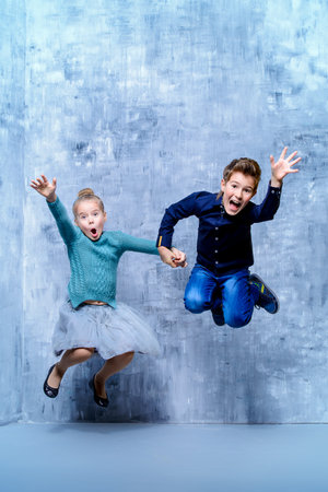 Kid's fashion. Two laughing children jumping for joy. Studio shot. Clothes for children.の写真素材
