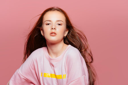 Teen style. Beautiful young model with long hair posing at studio in jeans and pink sweatshirt....