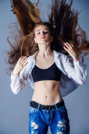 Teen style. Beautiful young model with long hair posing at studio in jeans and white shirt. Beauty, fashion.の写真素材