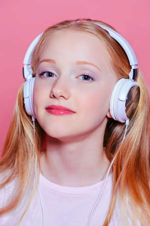 Portrait of a cute modern girl teenager with headphones over pink background. Studio shot. Teen's fashion.の写真素材
